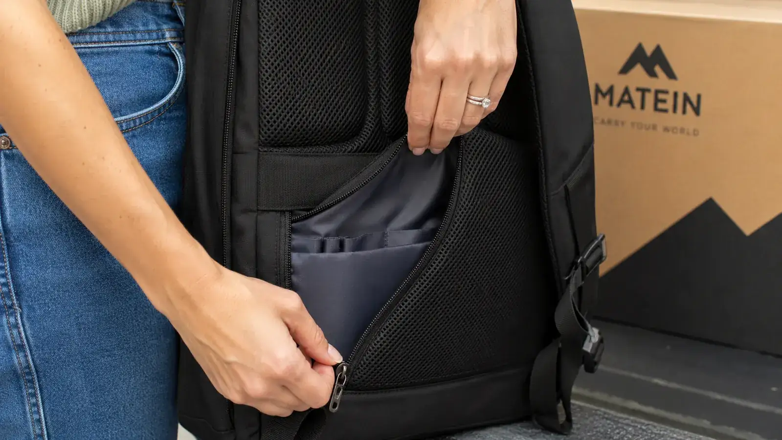 Close-up of hands opening a hidden back-panel zipper on a dark travel backpack