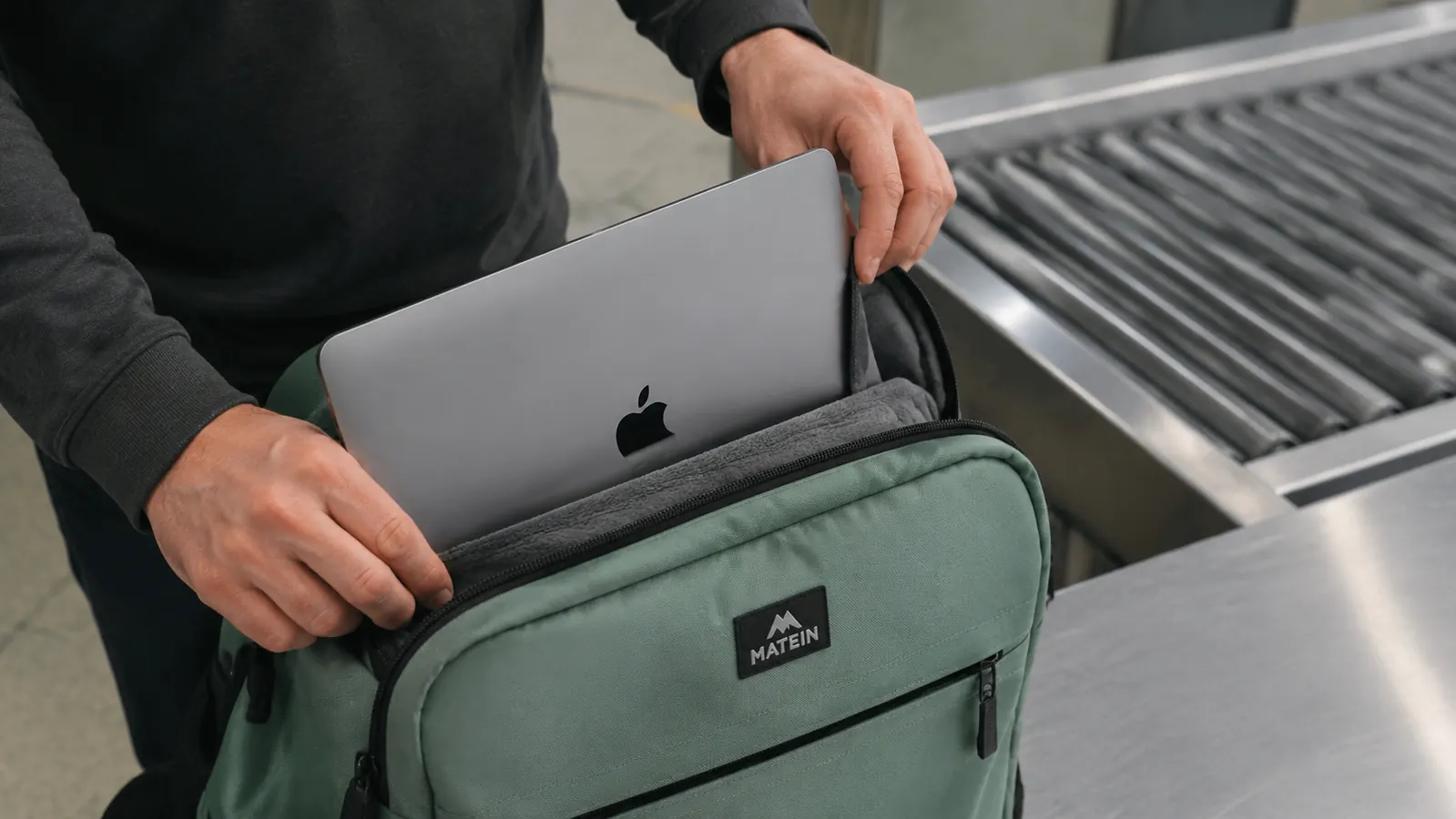 Laptop being slid out of a padded TSA-friendly compartment on a travel backpack at an airport security lane