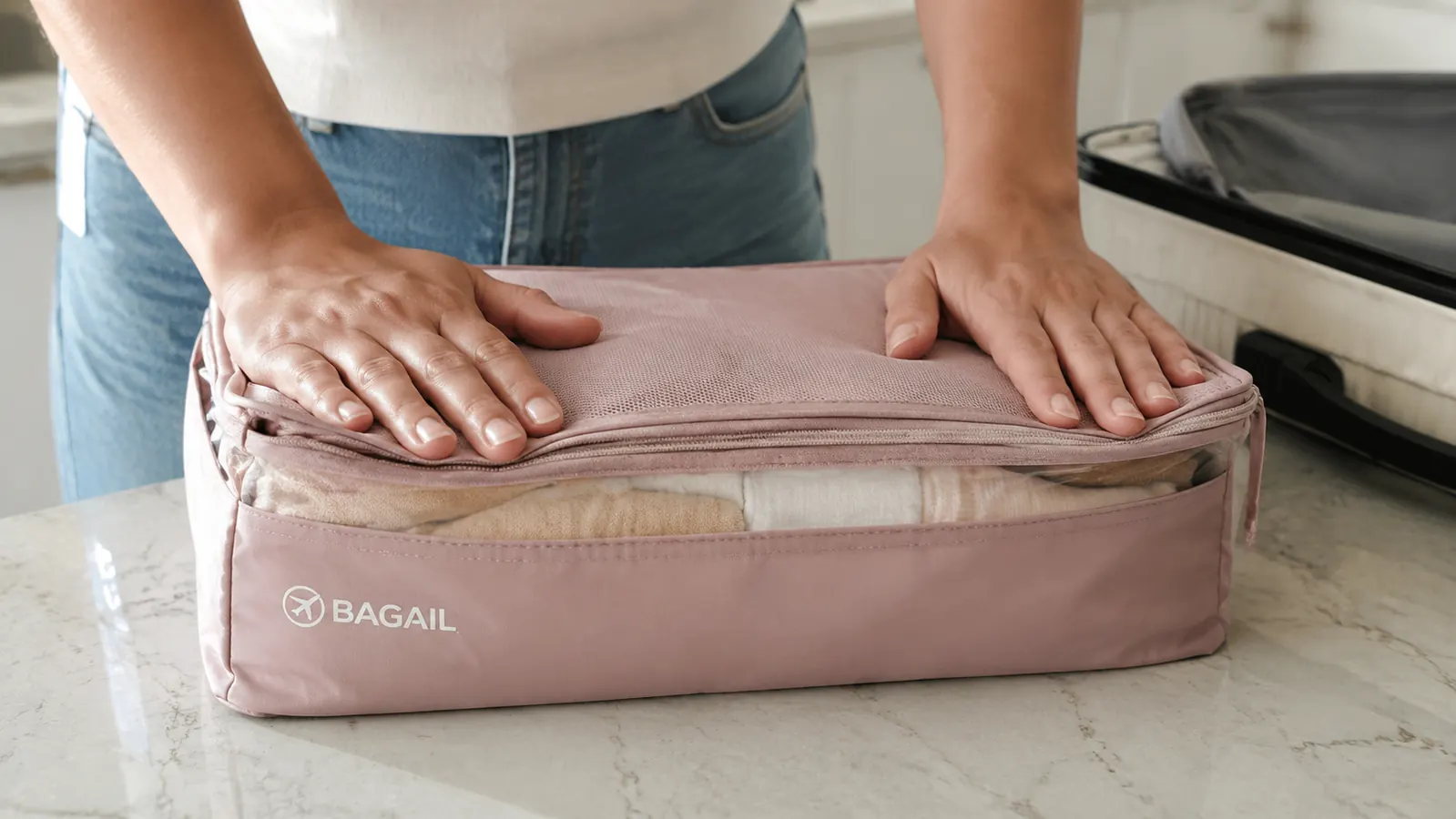 Hands compressing a packing cube by pressing down on the top zipper panel to flatten it