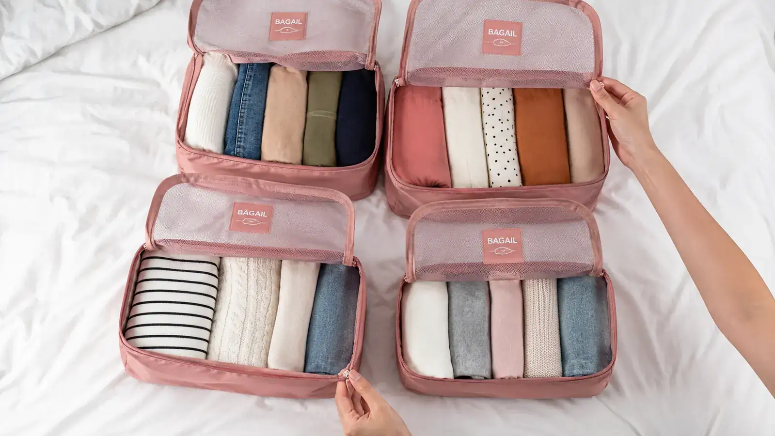 Overhead flat-lay of clothes sorted into BAGAIL compression cubes by category, tops in one, bottoms in another