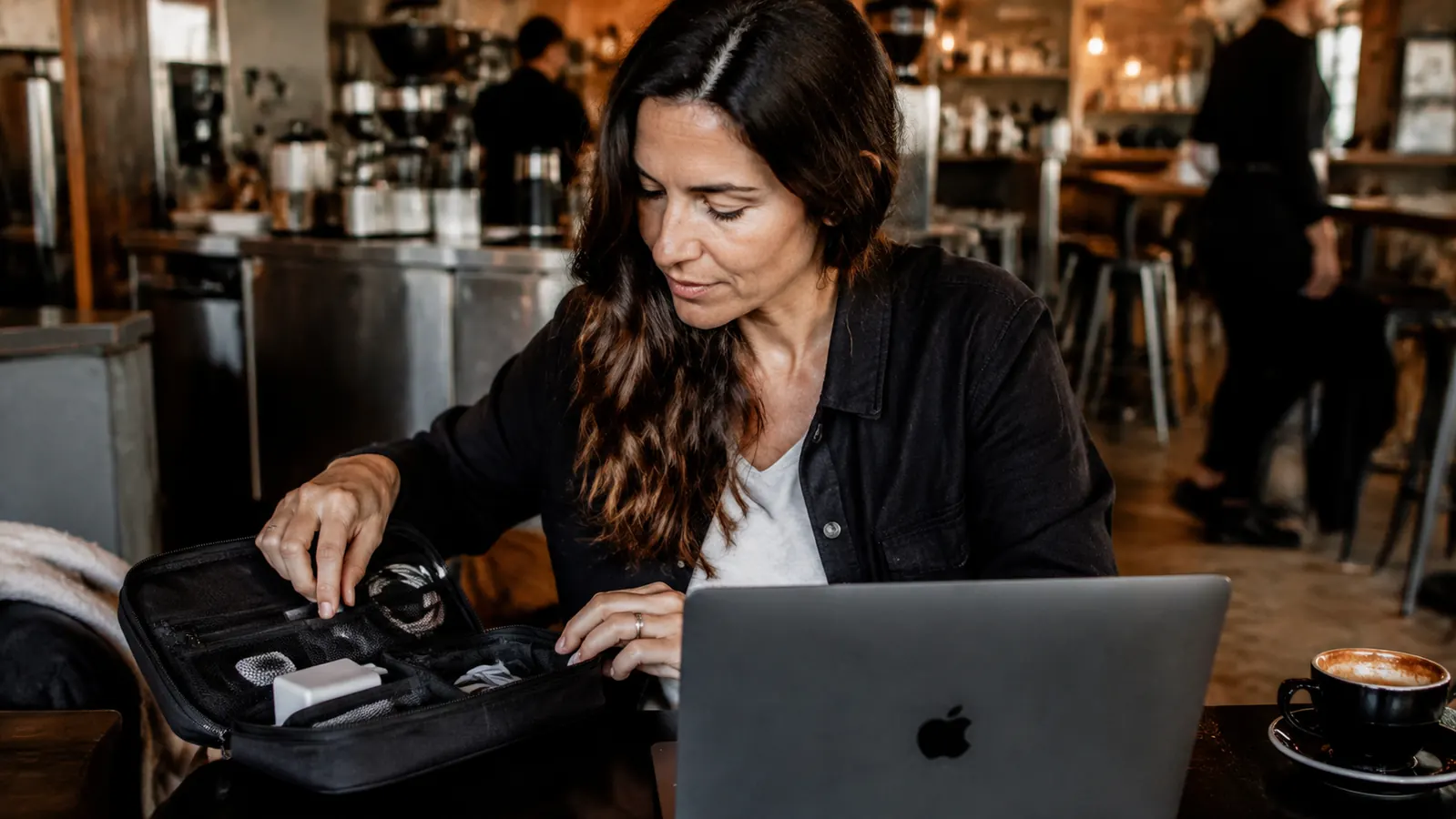 Traveler pulling a cable from an organized pouch at a cafe table without looking inside