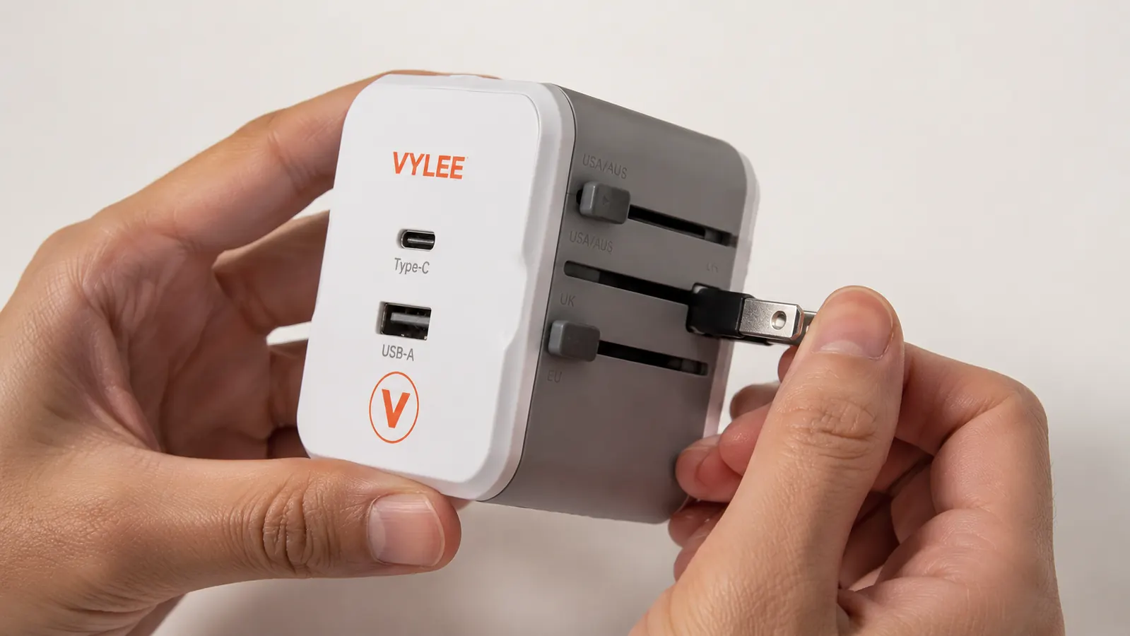 A hand holding the VYLEE travel adapter showing the sliding plug prongs and port labels