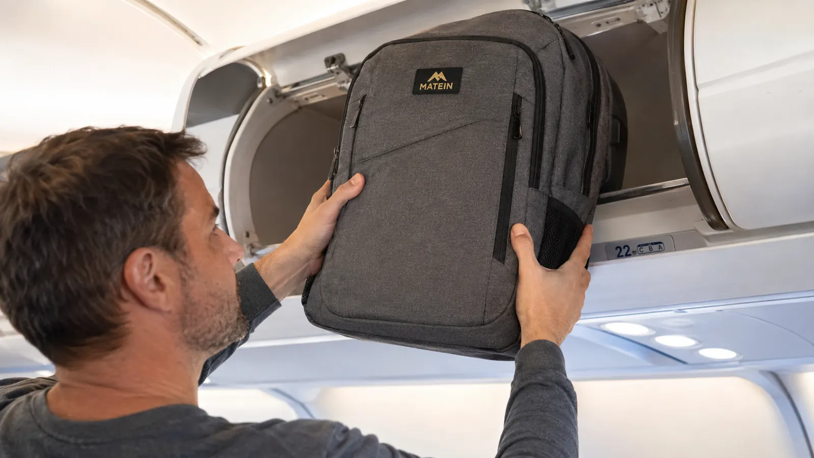 Traveler pulling the MATEIN backpack from an overhead bin on an airplane
