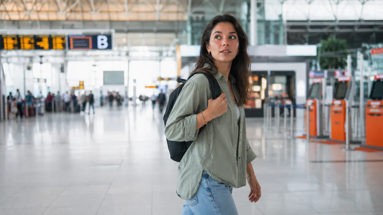 Confident woman walking through a bright airport terminal with only a backpack as carry-on luggage