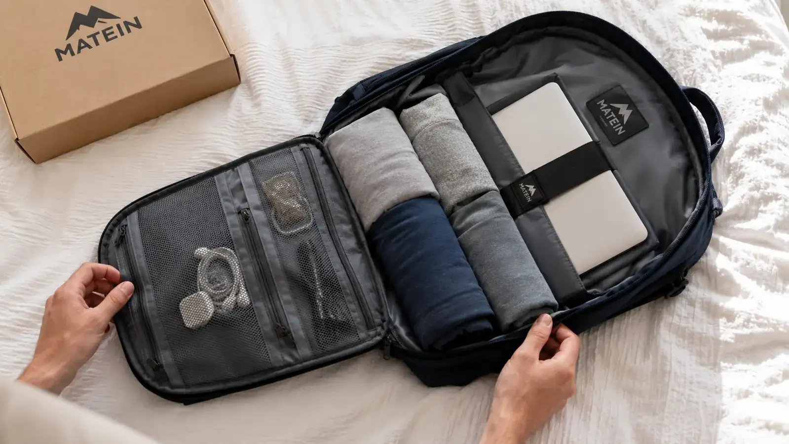 Open MATEIN backpack laying flat showing all interior compartments with a 15-inch laptop, cables, and clothing organized inside