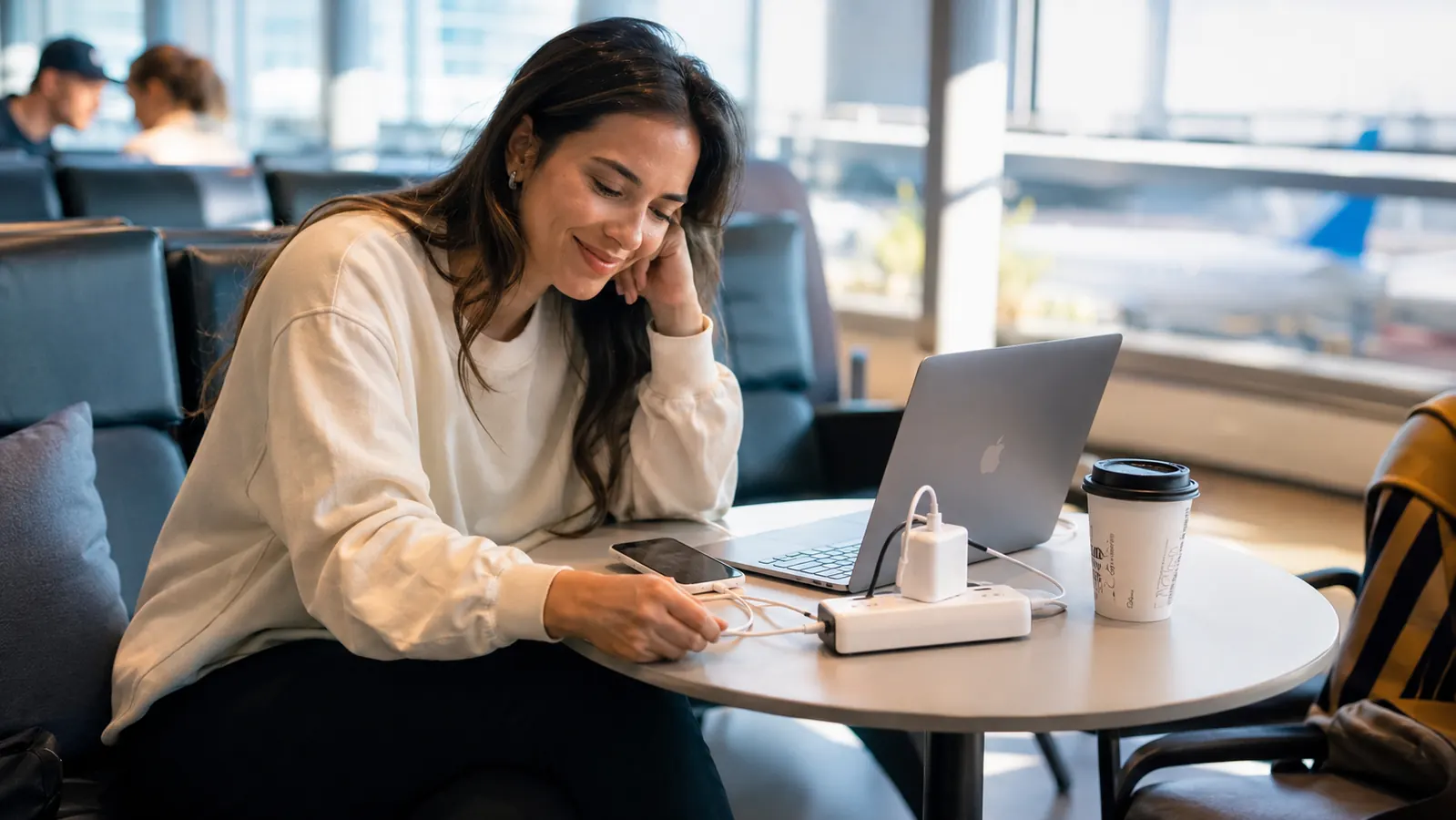 Woman relaxing in an airport lounge charging multiple devices from a single adapter