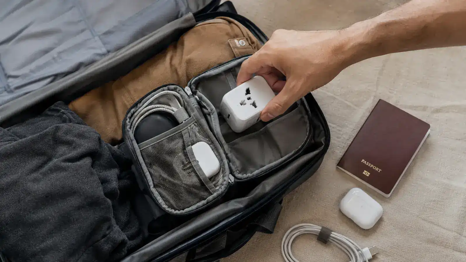 Traveler packing a VYLEE adapter into a small electronics pouch inside a carry-on bag